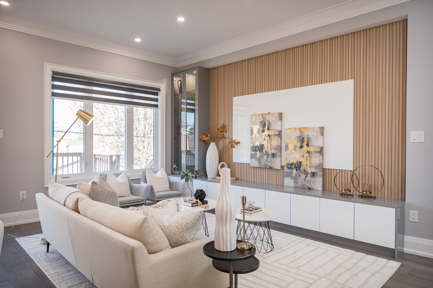 Bright contemporary living room with a cream sofa, neutral decor, wood slat accent wall, abstract art panels, and large window letting in natural light